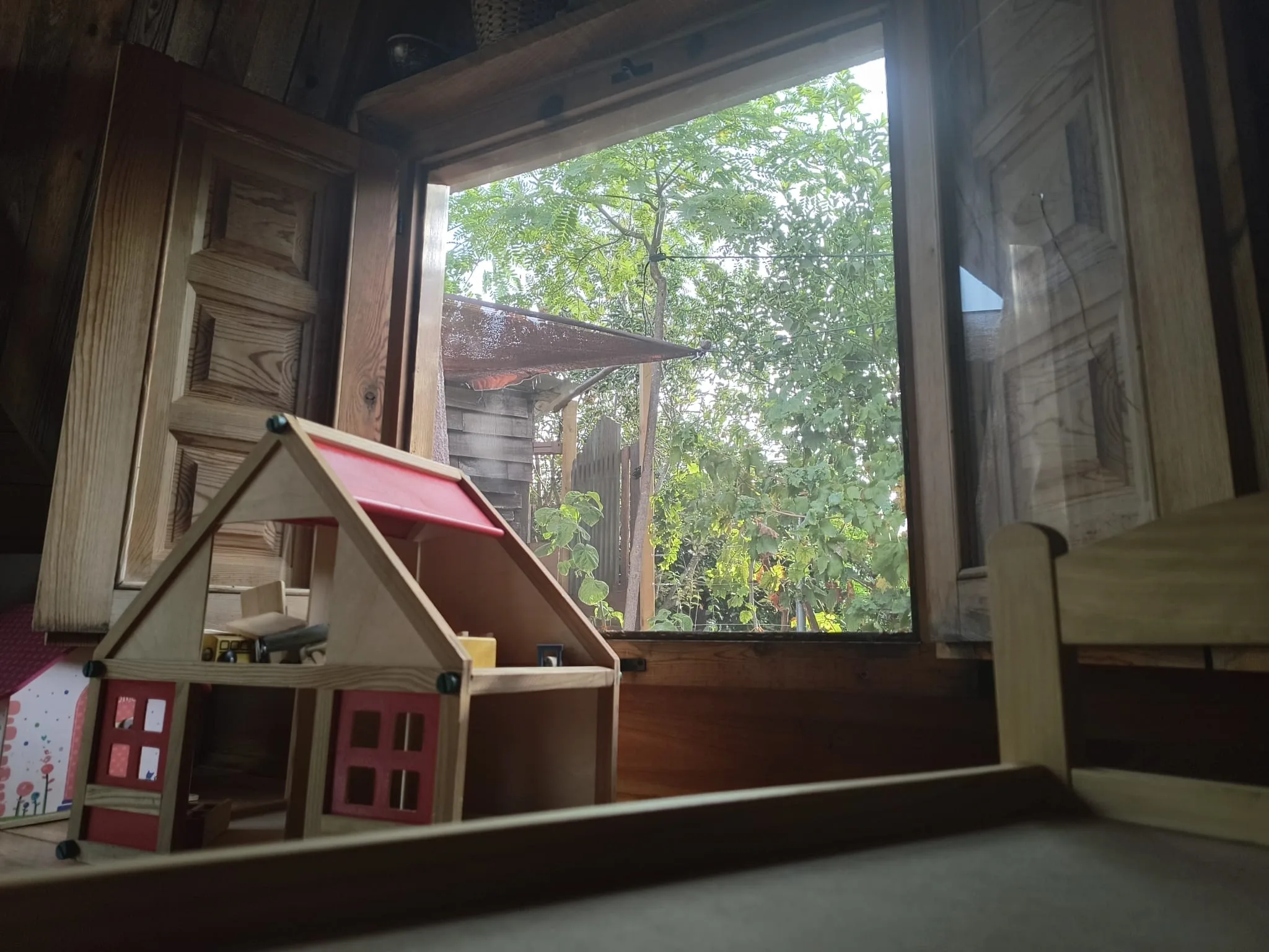 Ventana abierta con vistas a árboles y casita de madera para juego simbólico, conexión interior-exterior en nuestro espacio educativo.