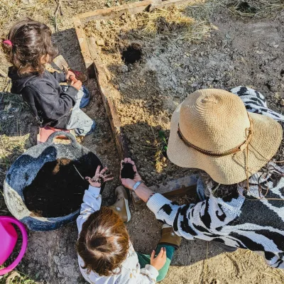 Actividades de huerto al aire libre varios niños y adulta preparan un bancal, hacen hoyos y añaden compost antes de plantar.