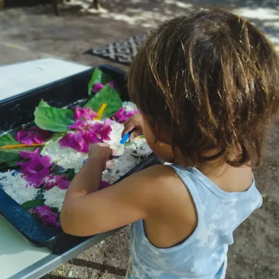 Actividades sensoriales al aire libre: niño manipula una bandeja con harina y flores, realiza trasvases con cucharas y explora texturas.