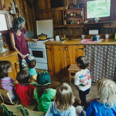 Actividades de cocina infantil una educadora prepara una receta en la estufa de una cocina de madera mientras los niños observan; hábitos saludables y autonomía.