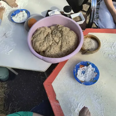 Actividades de cocina infantil: niños amasan harina y preparan masa de pan con semillas en mesas exteriores.