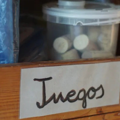 Primer plano de estante de madera rotulado “Juegos” con bote de corchos; organización de materiales en aula del domo de un centro en la naturaleza.