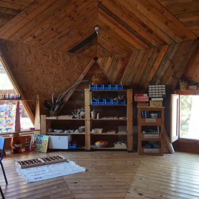 Estanterías con materiales Montessori, mesa infantil y ventanales triangulares que iluminan el aula de un centro en la naturaleza.