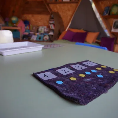 Mesa redonda con tapete de conteo (números 1–4 y fichas de colores) en aula de domo geodésico; aprendizaje matemático en un centro en la naturaleza.