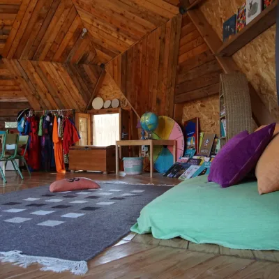 Rincón de lectura con cojines, estanterías y mesa infantil en domo geodésico; aprendizaje acogedor en un centro en la naturaleza.