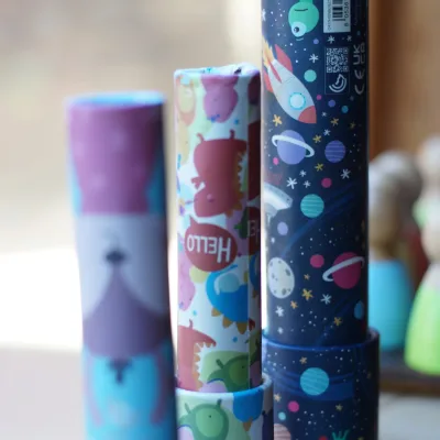 Primer plano de varios caleidoscopios de colores con dibujos de planetas, cohetes y animales sobre una repisa de madera, detalle del aula creativa en el centro en la naturaleza.