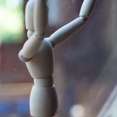 Primer plano de un maniquí articulado de madera para dibujo, con los brazos en alto, sobre soporte metálico y frente a una ventana con luz natural; detalle del aula creativa del centro en la naturaleza.