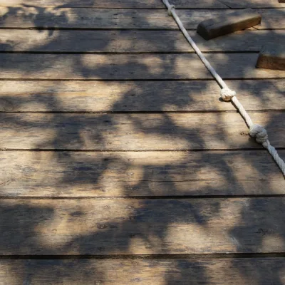 Detalle de la rampa de escalada en madera con cuerda y presas, bajo luz y sombra de los árboles; parte de la zona cabaña-rocódromo del centro en la naturaleza.