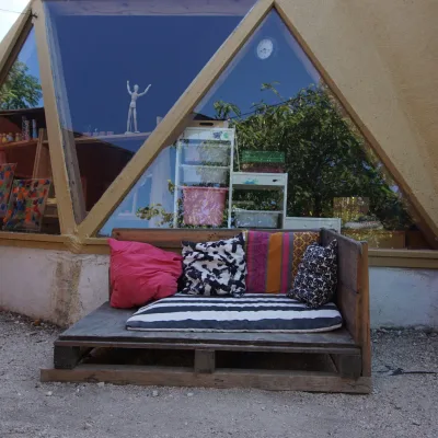 Sofá de palets con cojines multicolor frente a ventanales triangulares del domo; se ven pinturas infantiles y reflejos de árboles en este centro en la naturaleza.